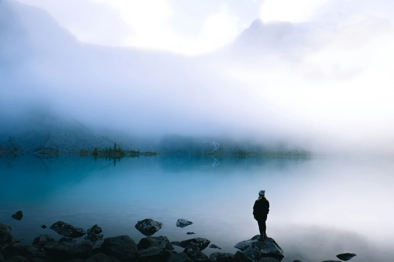 a man standing on a lake shore near some mountains