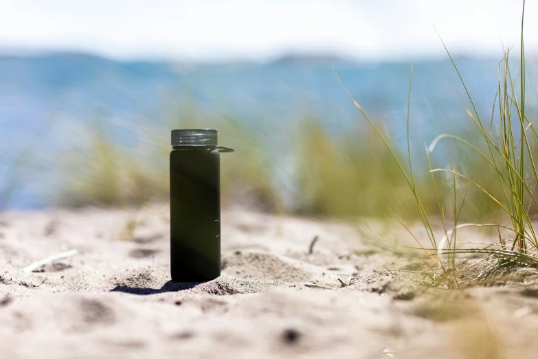 a small black water bottle sitting in the sand