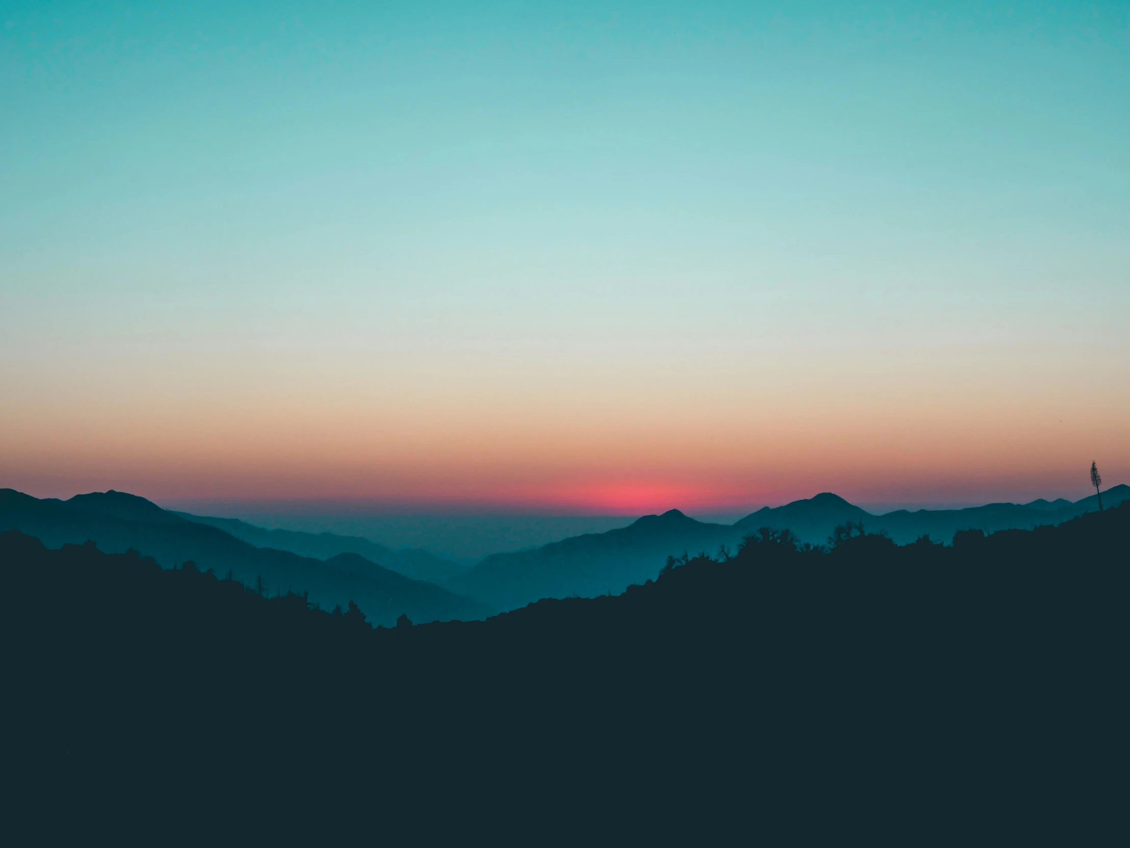 the sun set on a mountain range with silhouetted trees