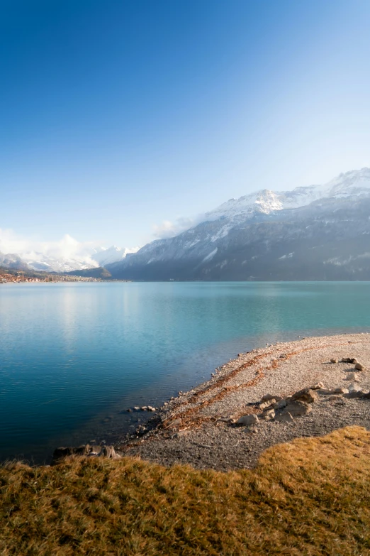 a lake surrounded by mountains and grass in the daytime