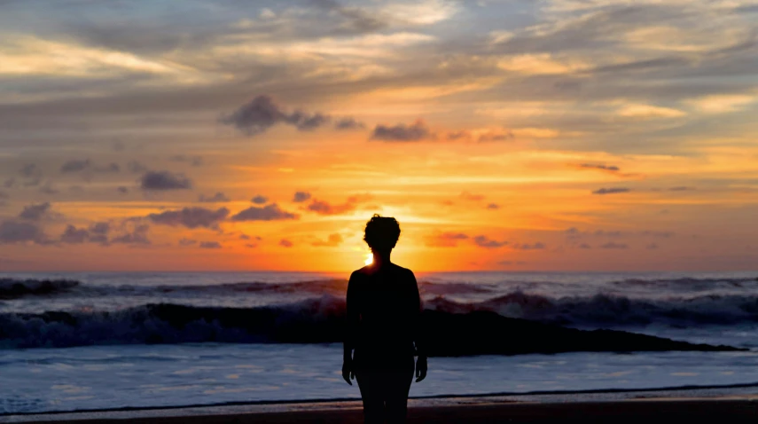 a person is standing on the beach at sunset