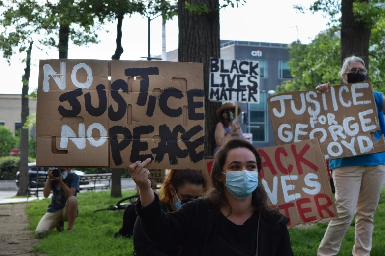 protesters holding protest signs at park on a cloudy day