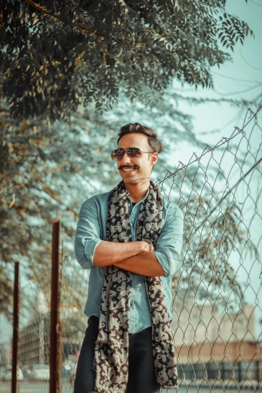 a man with his arms crossed standing in front of a fence