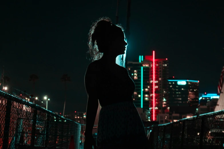 the dark image of a young woman standing outside with city lights behind her