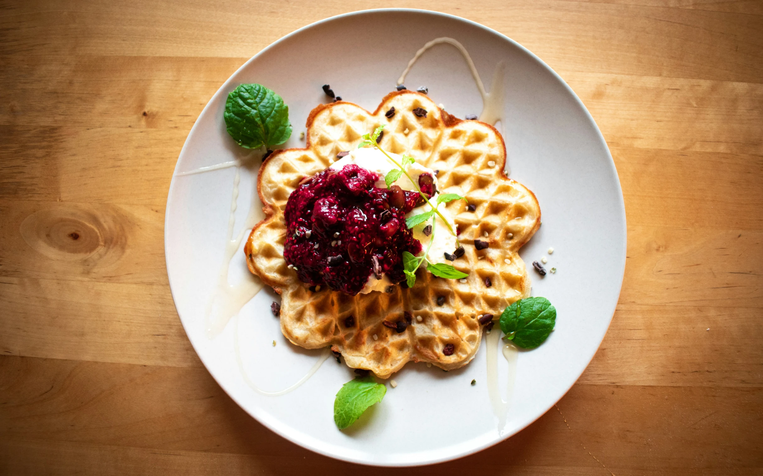 a white plate with two waffles covered in beetroot and a garnish