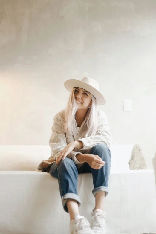 woman with white hat, blue jeans and sneakers sitting on couch