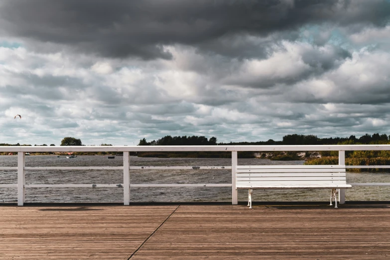 a white bench is on a wooden dock by the ocean