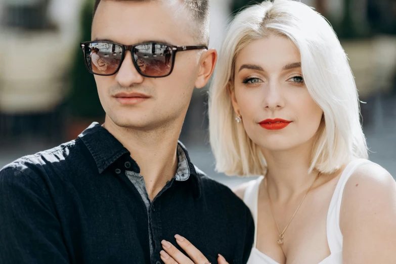 a man in a white dress shirt standing next to a woman with a blonde hair and glasses