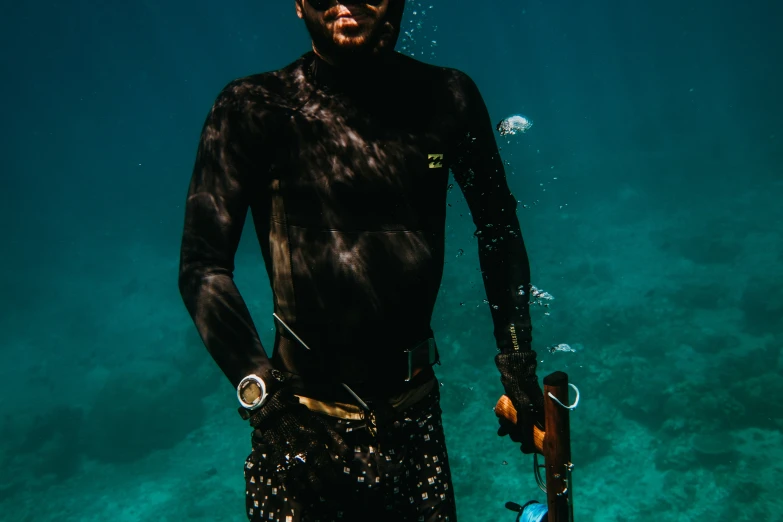 man in black wet suit holding a fishing rod under water