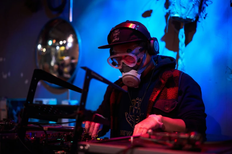 a dj mixes while wearing a mask, headphones, and a hat