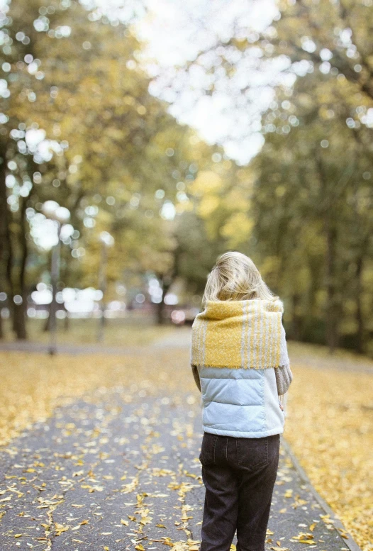 a young child stands on an asphalt road that is lined with trees and leaves