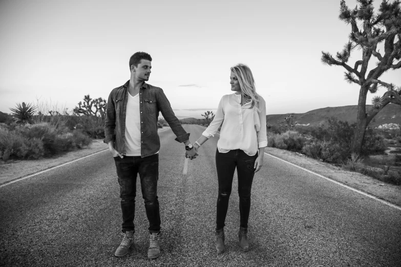 a man and woman walking in the road while holding hands