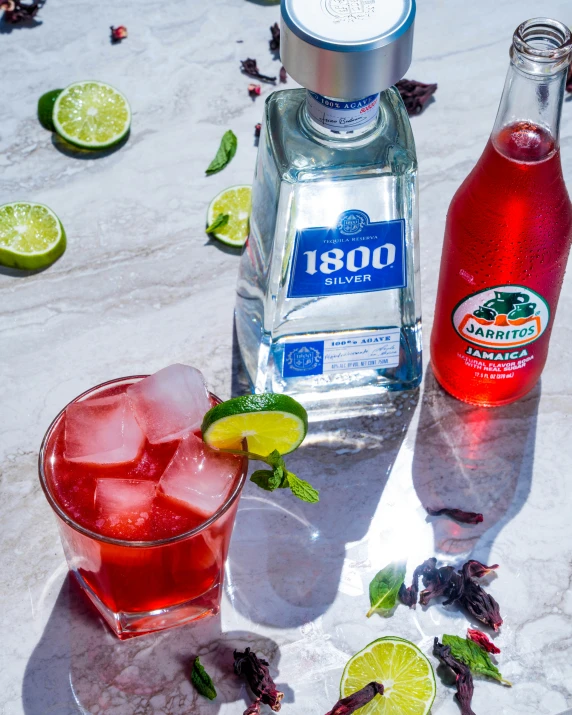 a glass with red liquid sits next to bottles