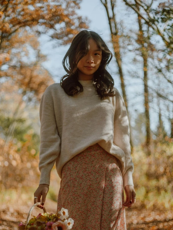 a woman wearing a sweater and flower skirt holding flowers