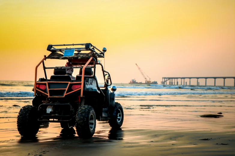 a four wheeled vehicle on beach with pier in background