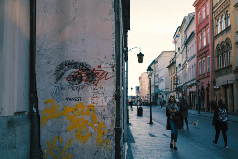 some people are walking down the street with graffiti on the wall