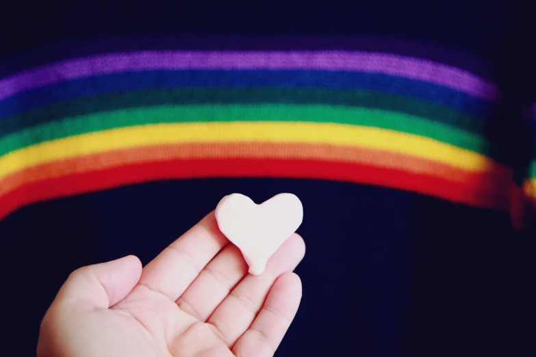 a hand holding a white heart on a colorful background