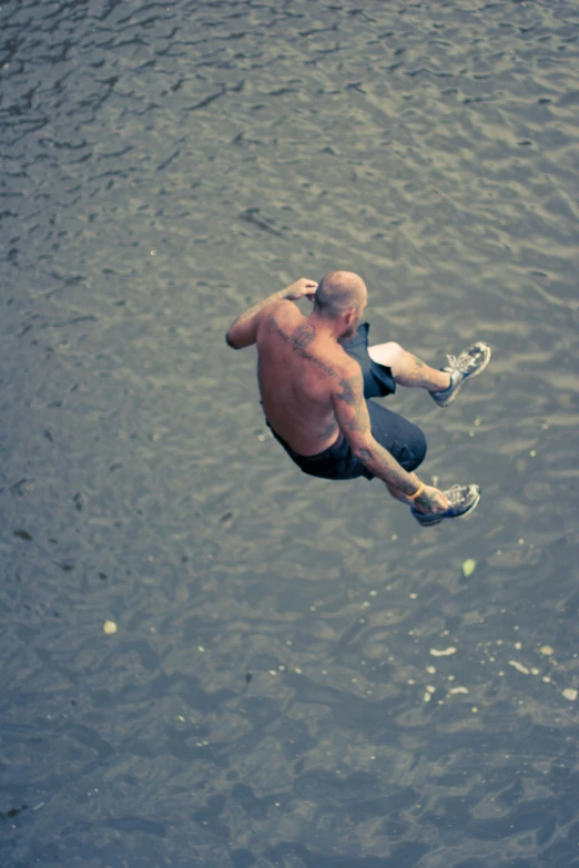 man diving with his feet in the water and a frisbee flying over him