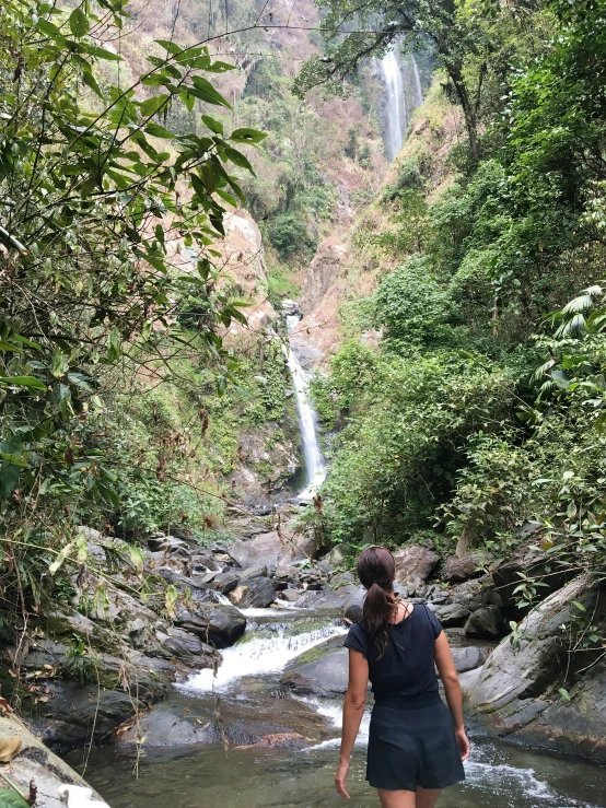 the woman is walking through the stream towards a waterfall