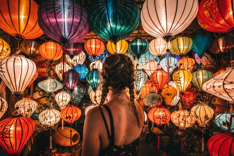 the back of a woman standing near many lit up chinese lanterns