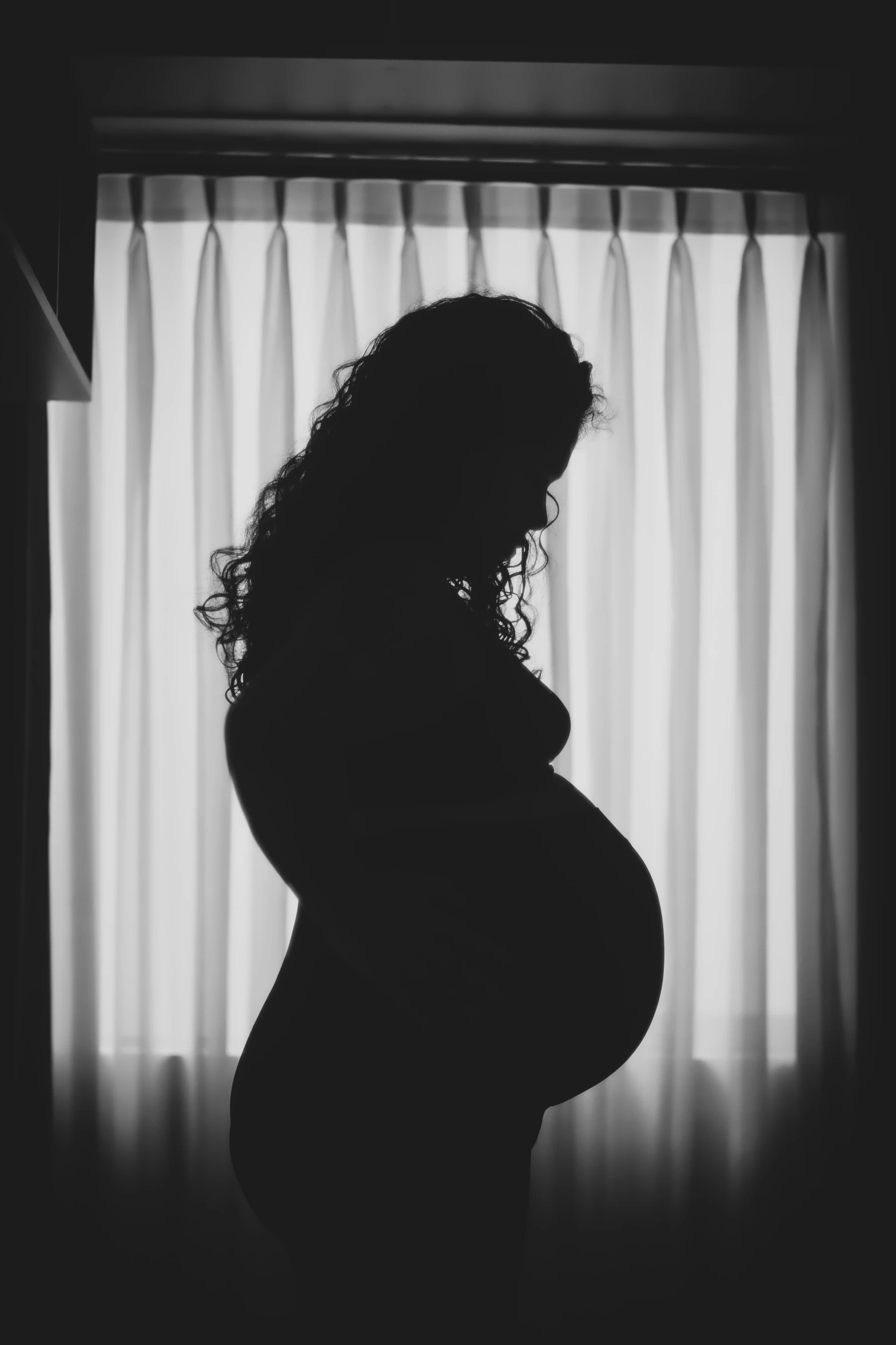 the silhouette of a pregnant woman in front of a curtain