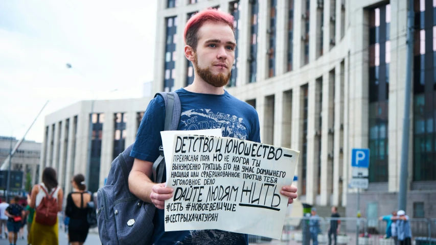 a bearded man holding a sign in front of a building