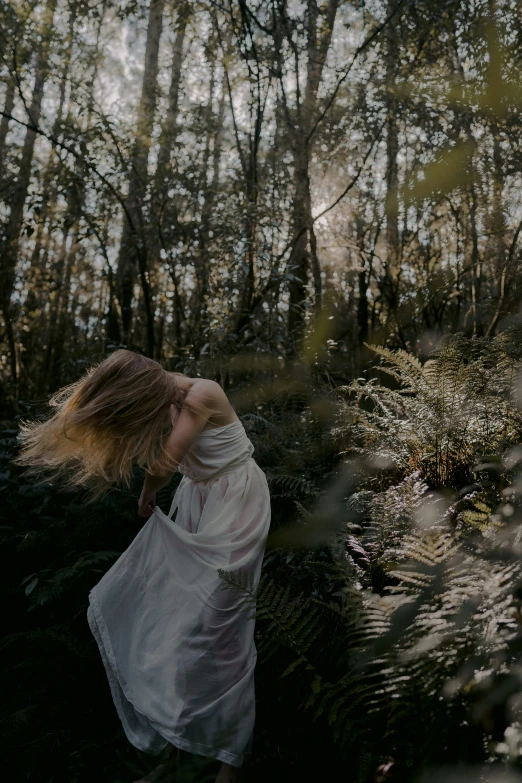 a woman wearing white is walking in a forest