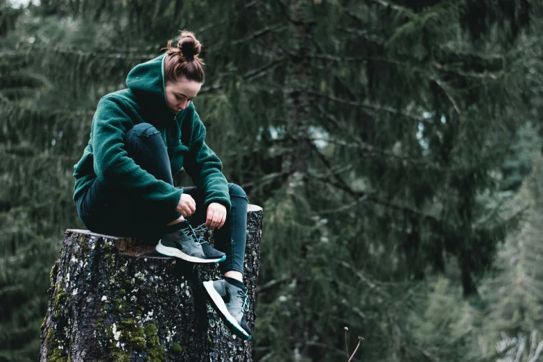 woman sitting on edge of tree stump in forest