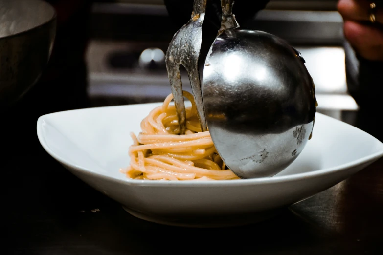 the spoon is holding up noodles on a plate