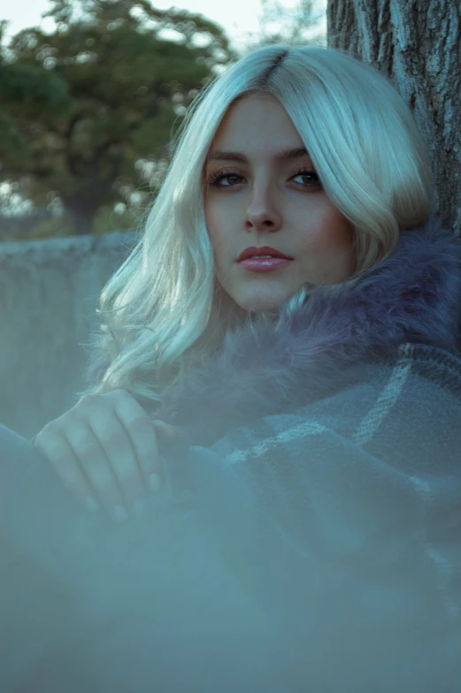 a woman wearing a coat with a fur collar standing near a tree