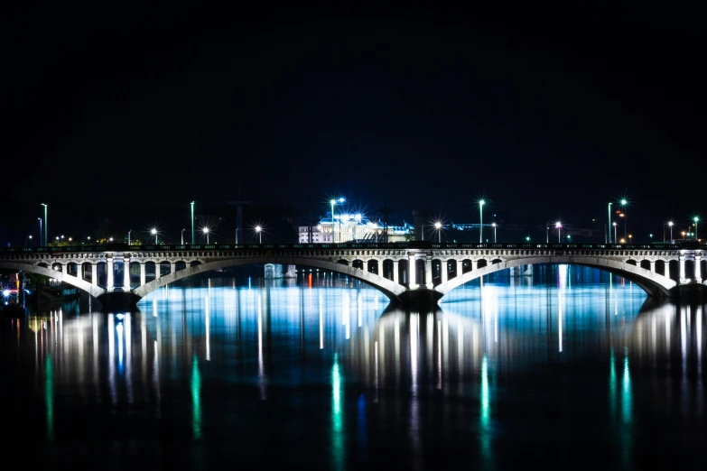 a bridge is illuminated by night with lights reflecting on the water