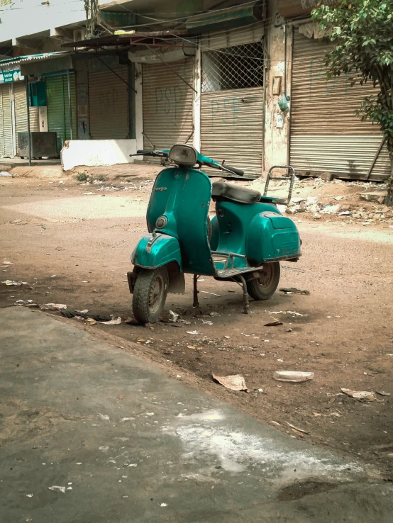 an old green scooter parked in a dirty lot