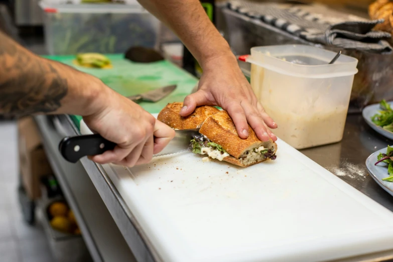 person using knife to slice a sub sandwich off a  board