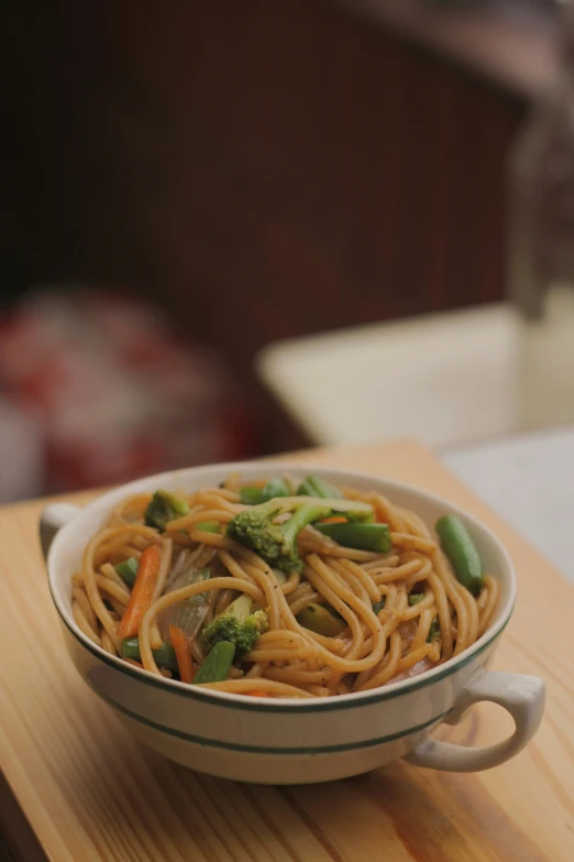 a white bowl of noodles and broccoli on a wood table