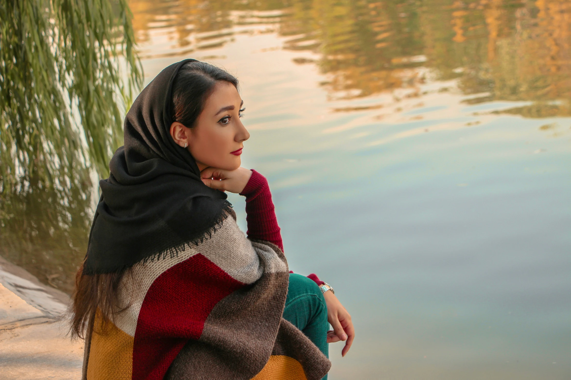 a woman in black, yellow and brown sitting by water