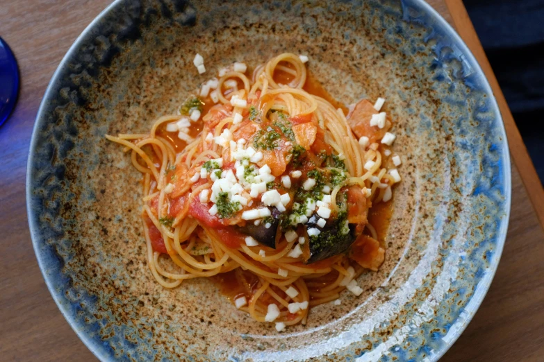 an empty blue bowl is filled with spaghetti with tomatoes