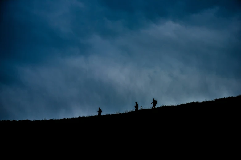 silhouettes of three people on a hill with dark blue sky