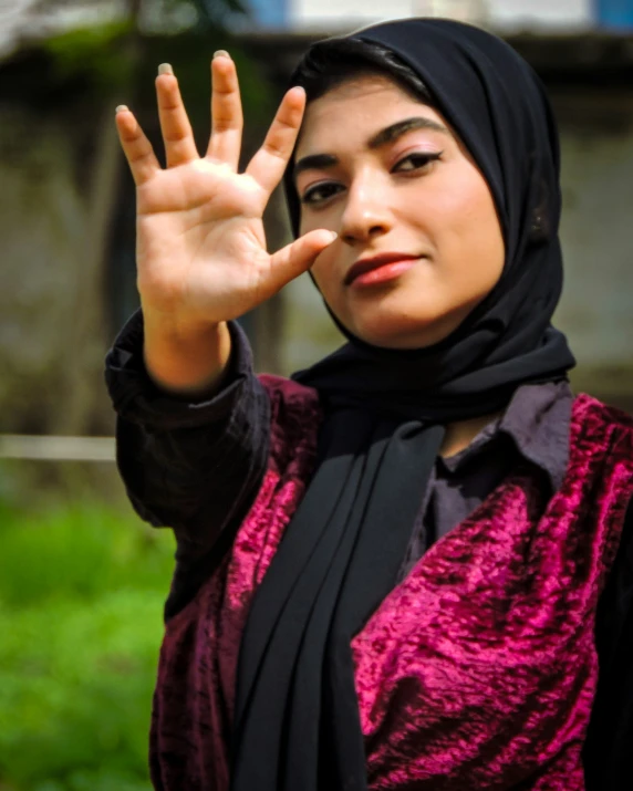 a woman wearing a hijab standing with her hand in the air