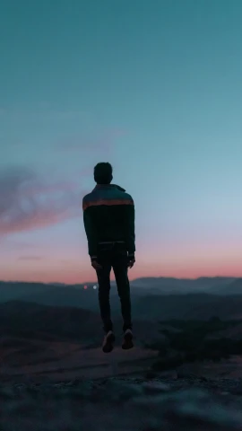 a man is standing on the edge of a hill watching the sun rise