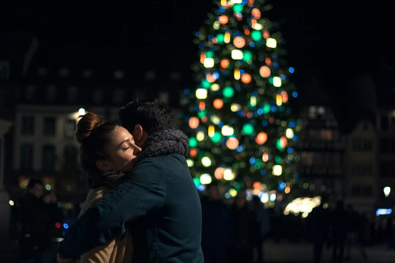 two people hug before a brightly lit christmas tree