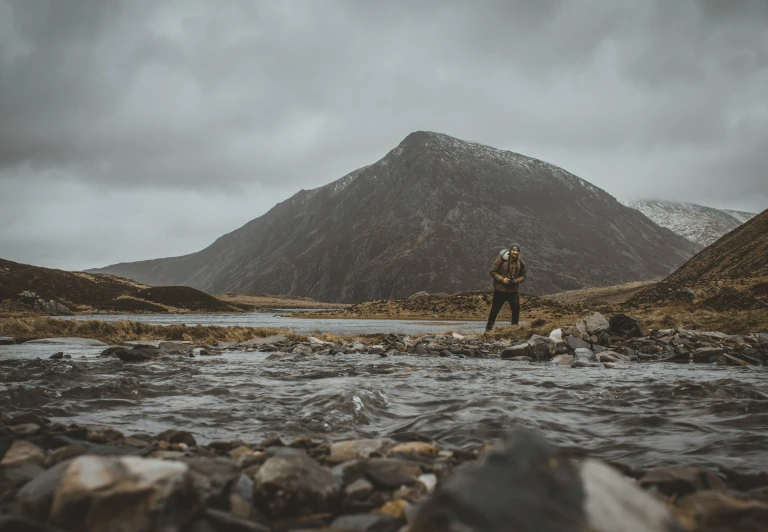 a person standing on rocks near the water in front of a mountain