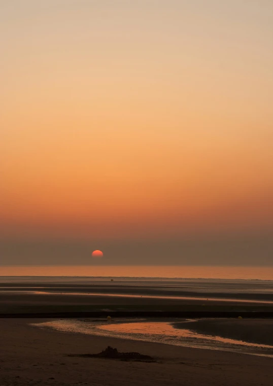 the sun is setting on a hazy day at the beach