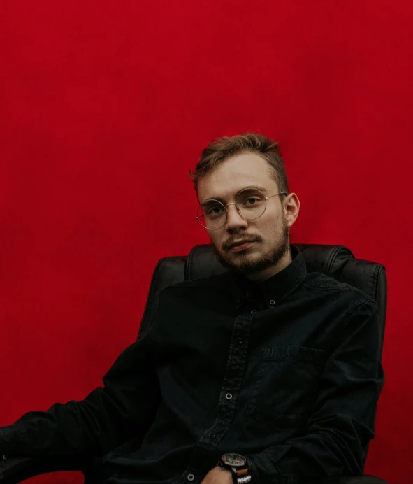 a man sitting in a chair against a red wall