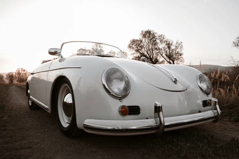 a white classic car with the roof down is sitting on a country road