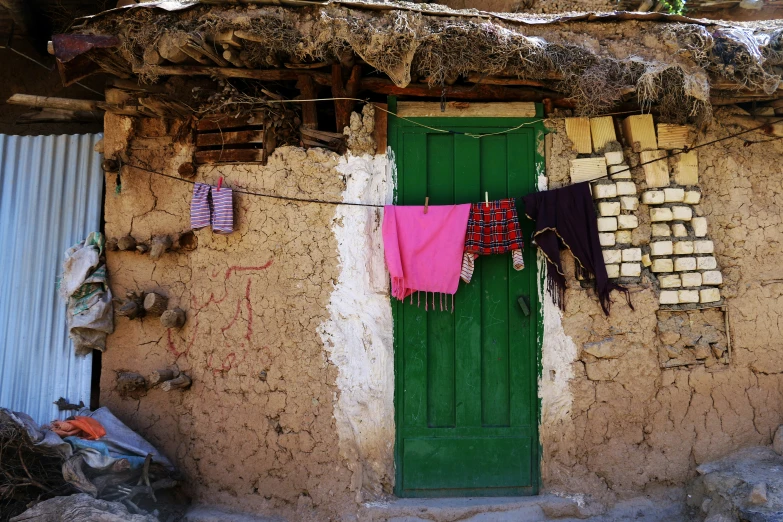 an entrance to a rustic home that has a green door and hanging towels