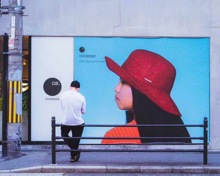 the man is walking down the sidewalk behind a billboard