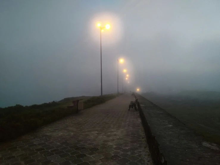 a walkway with foggy, light - colored lanterns and two people on motorcycles