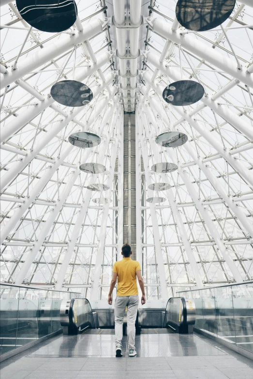 a man in yellow shirt walking under a large glass structure