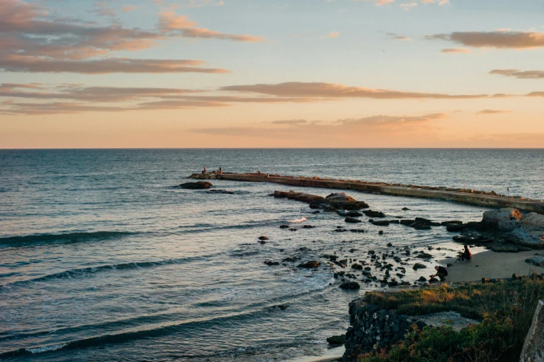 an orange sunset over the ocean with a couple of men and women on the rocks