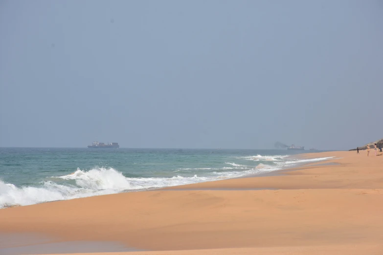 an ocean side beach with waves in front and a barge in the distance